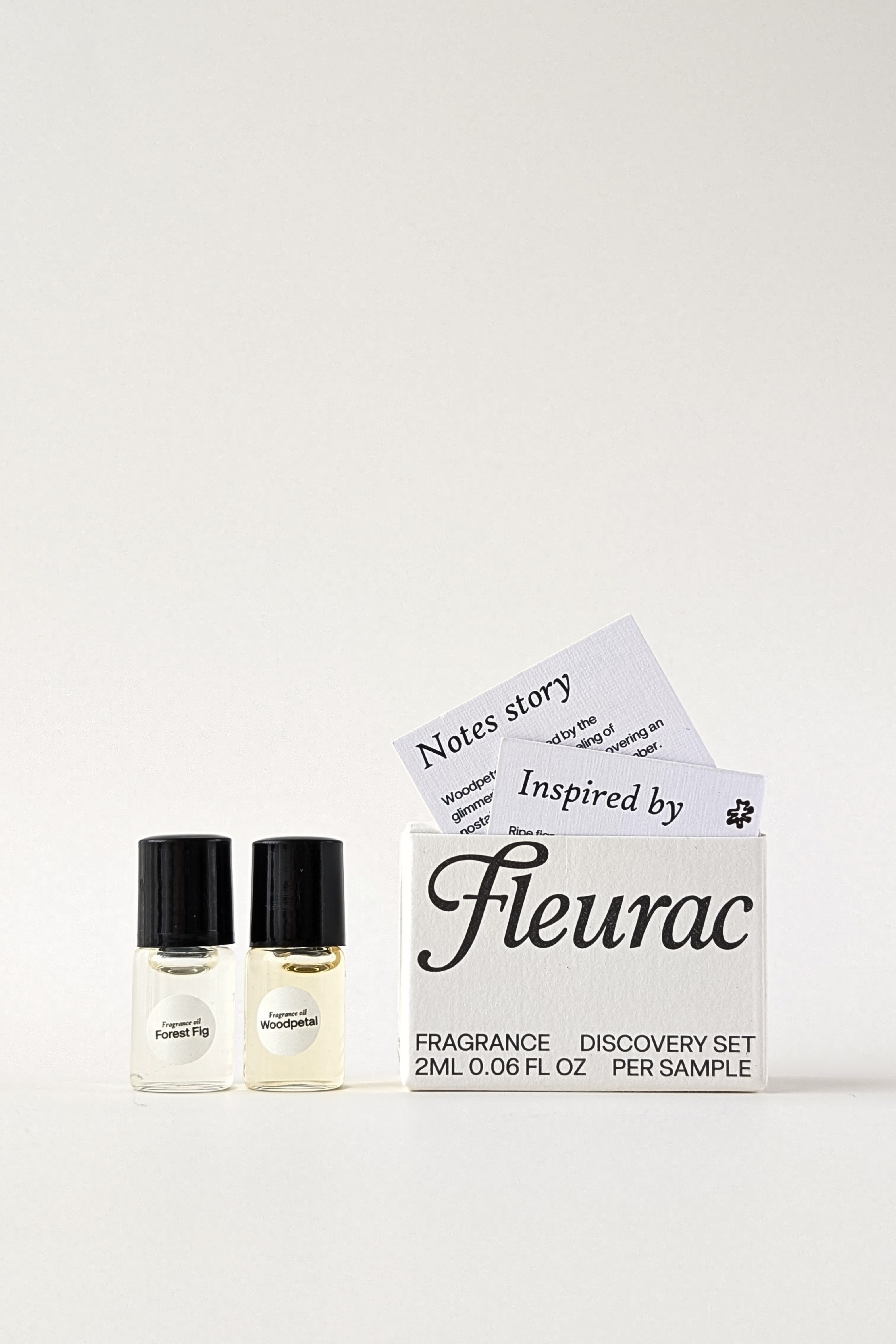 A clean oil perfume discovery set featuring two small glass sample bottles with black caps and a white box labeled 'Fleurac Fragrance Discovery Set'. A folded card behind the box reads 'Notes story Inspired by Fleurac'.