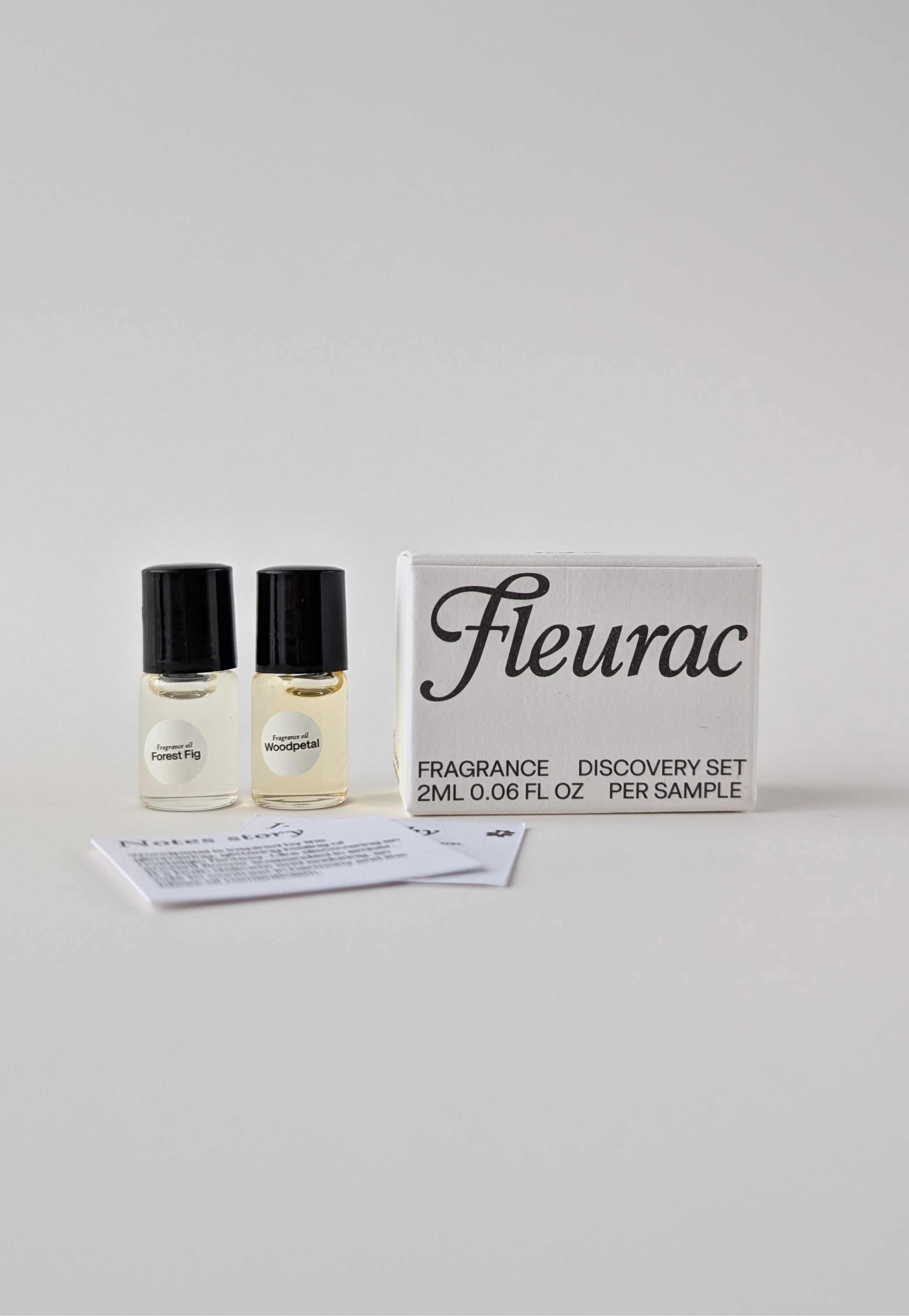 Fleurac fragrance clean oil perfume discovery set containing two 2ml sample bottles with black caps, a white notes card of what each perfume smells llike, and a white box with black text, photographed on a light gray background.